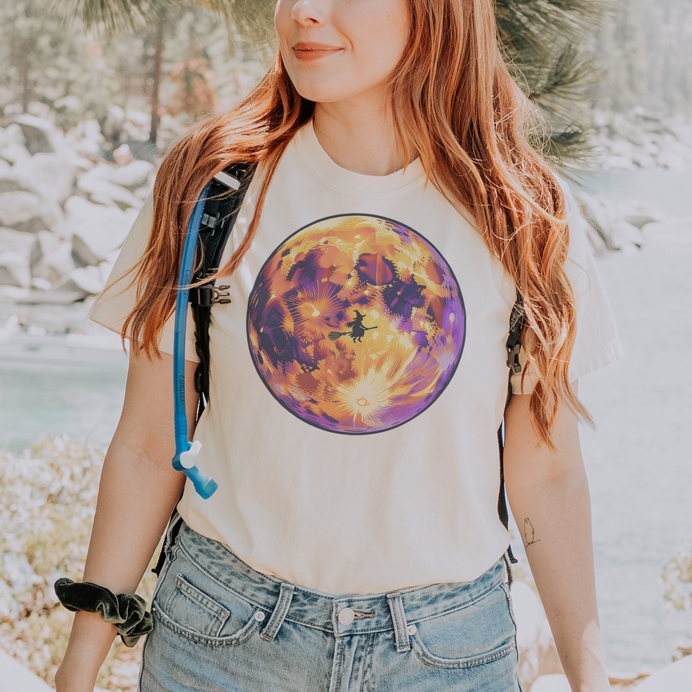 Witch Riding Broomstick Across a Glowing Textured Moon Tee